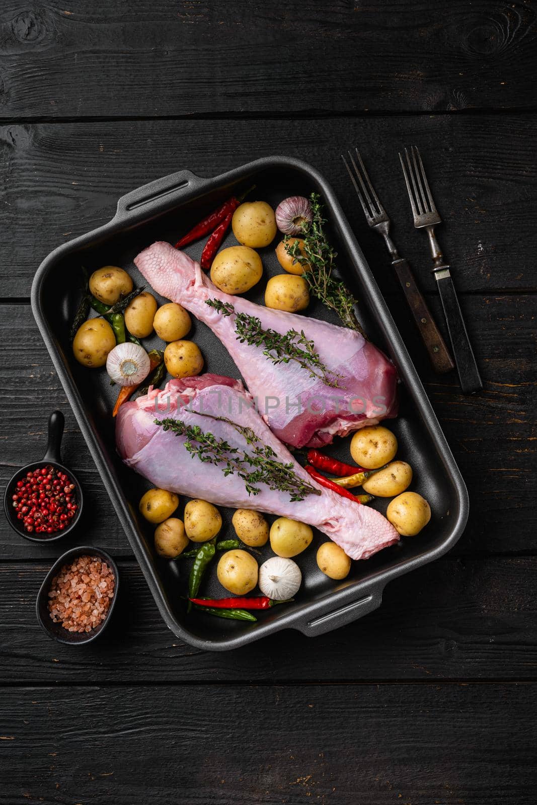 Raw turkey drumsticks with thyme, pepper set, on black wooden table background, top view flat lay, with copy space for text