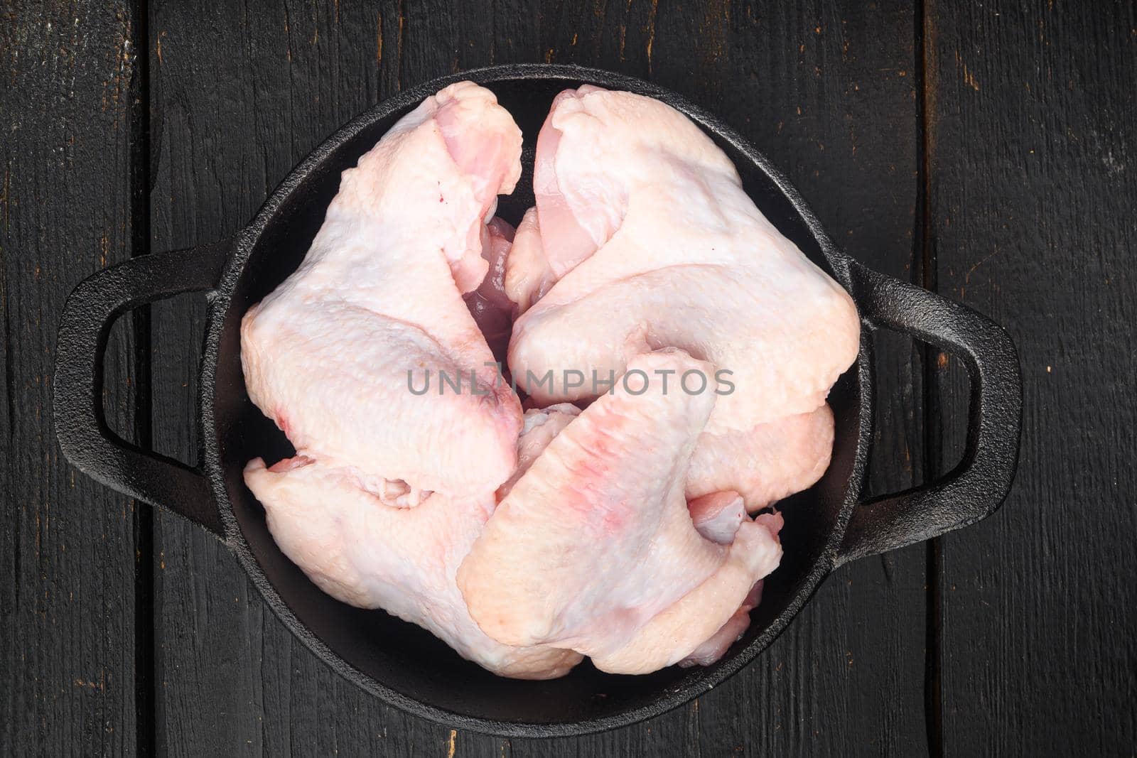 Uncooked chicken wings, in frying cast iron pan, on black wooden table background, top view flat lay by Ilianesolenyi