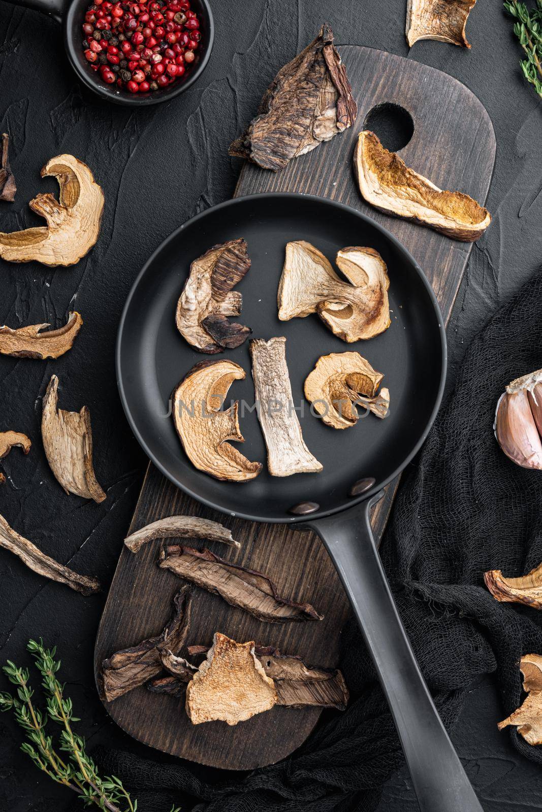 Dried mushrooms in cast iron frying pan, on black background, top view flat lay by Ilianesolenyi