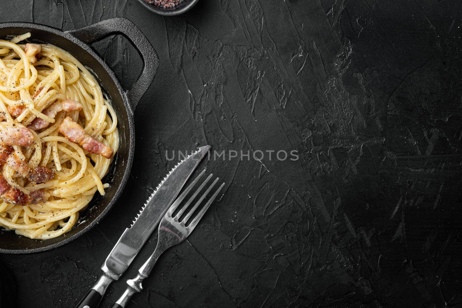 Pasta with egg sauce and ham, in cast iron frying pan, on black stone background, top view flat lay, with copy space for text by Ilianesolenyi