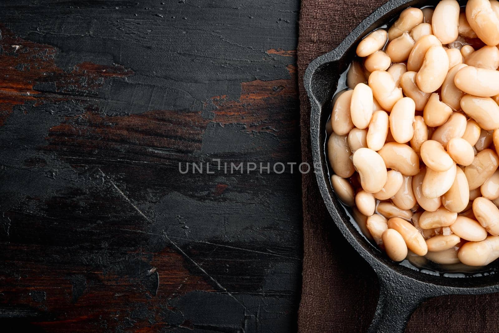 White kidney beans, in cast iron frying pan, on old dark wooden table background, top view flat lay, with copy space for text by Ilianesolenyi