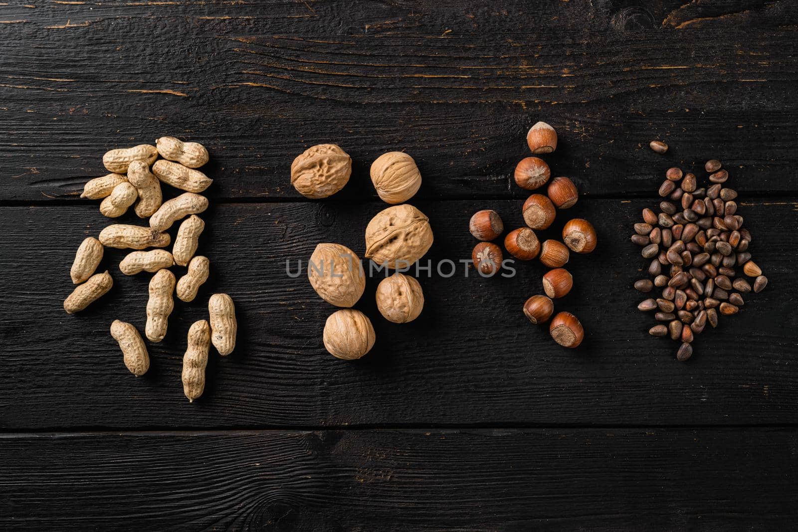 Mix of different nuts, peanut, walnut, pine nuts and hazelnut set, on black wooden table background, top view flat lay