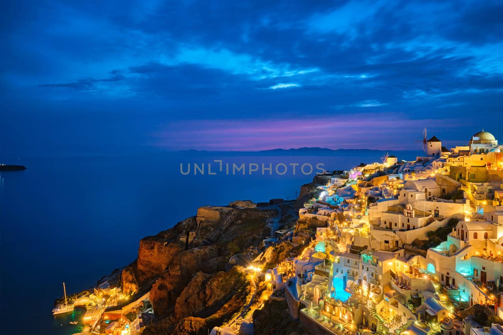 Famous greek iconic selfie spot tourist destination Oia village with traditional white houses and windmills in Santorini island in the evening blue hour, Greece