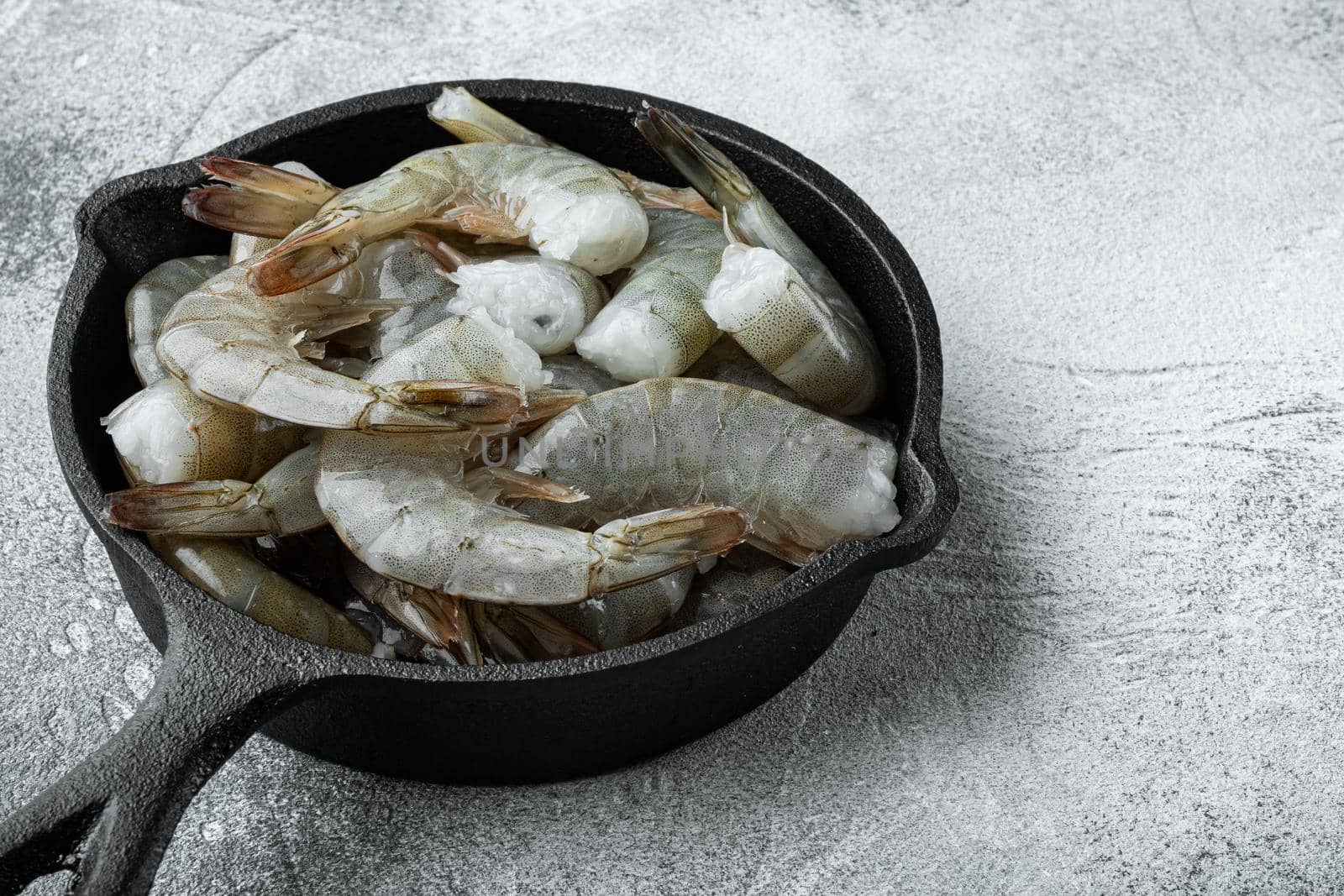 Raw tiger prawns, in cast iron frying pan, on gray stone background by Ilianesolenyi