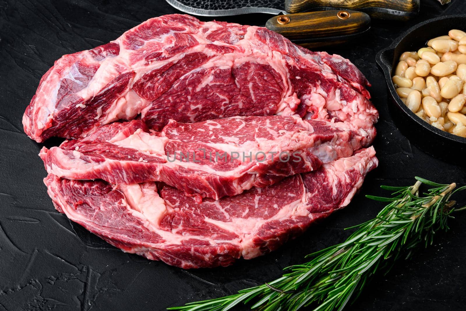 Raw Grass Fed Ribeye Steak with Salt and Pepper and herbs, on black stone background by Ilianesolenyi