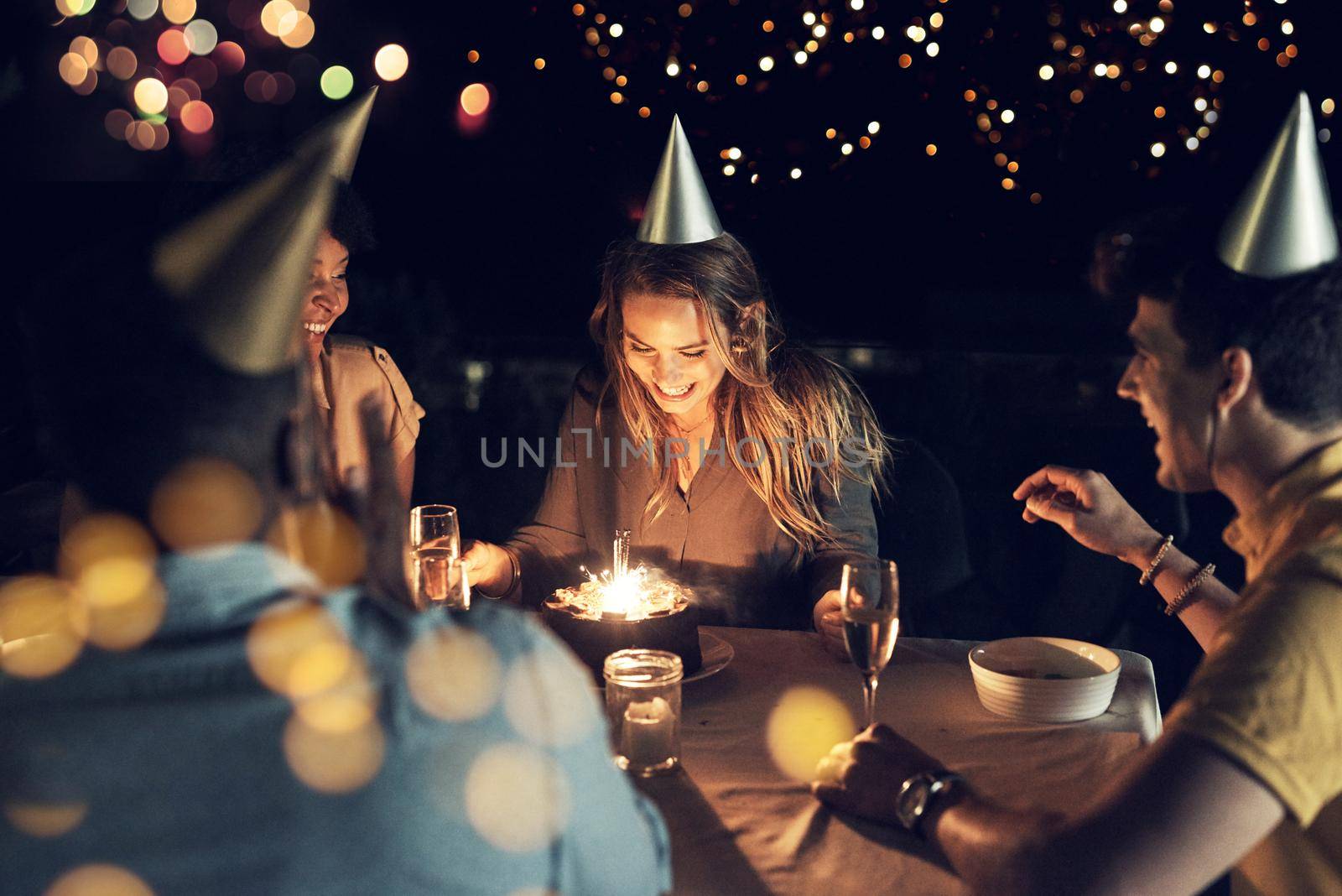 Shes celebrating her birthday with all her close friends. Shot of a group of friends celebrating a birthday together around a table at a gathering outdoors in the evening. by YuriArcurs