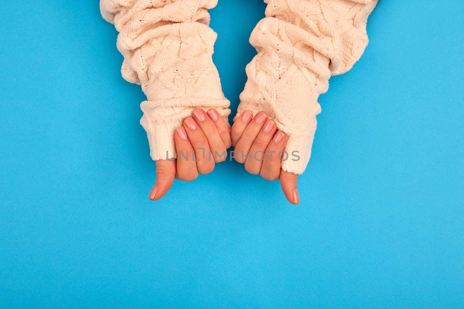 Neat manicure female hands sweater sleeves nude naturel on a blue background