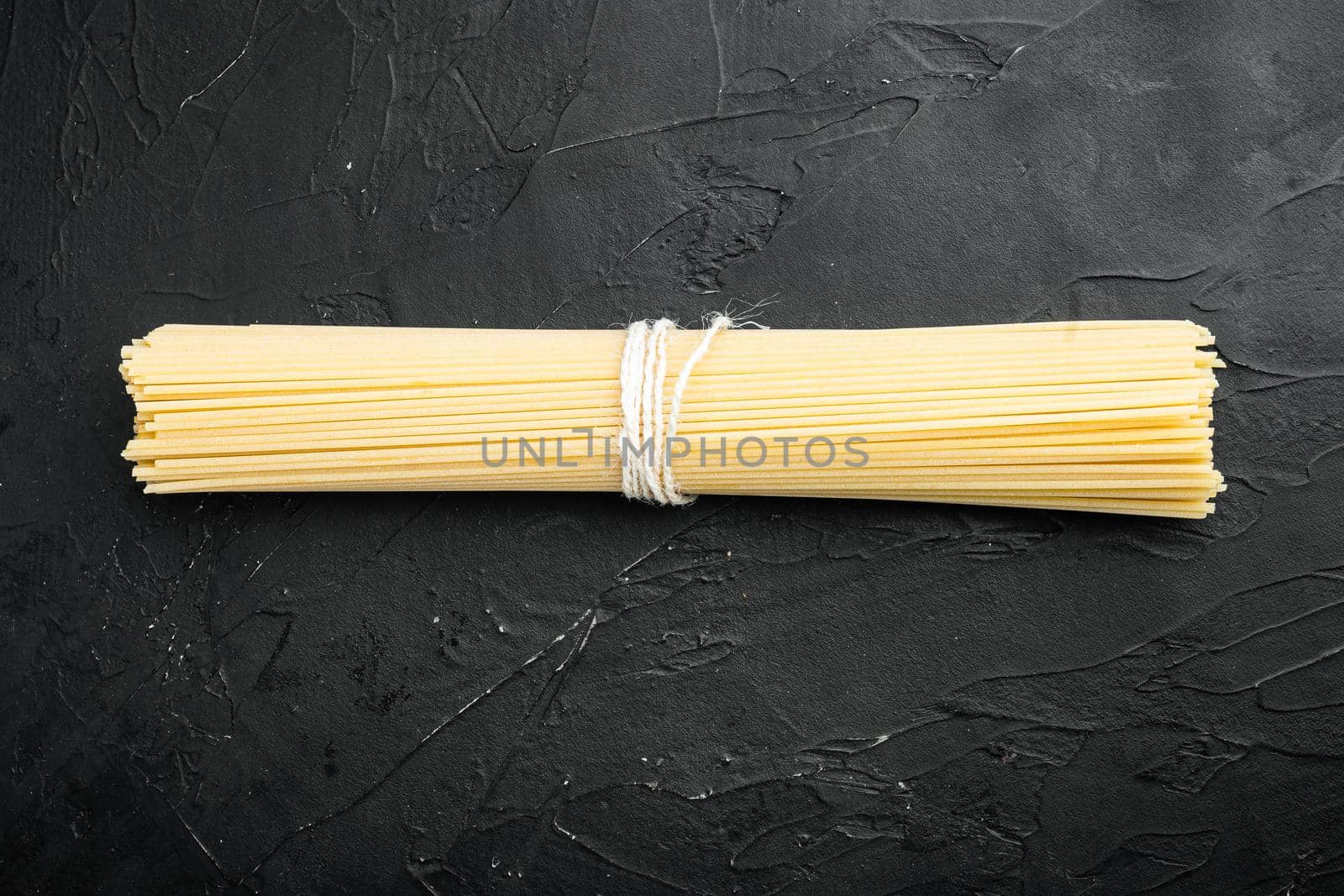 Wholemeal spaghetti ,Yellow long uncooked dried pasta, on black stone background, top view flat lay, with copy space for text by Ilianesolenyi