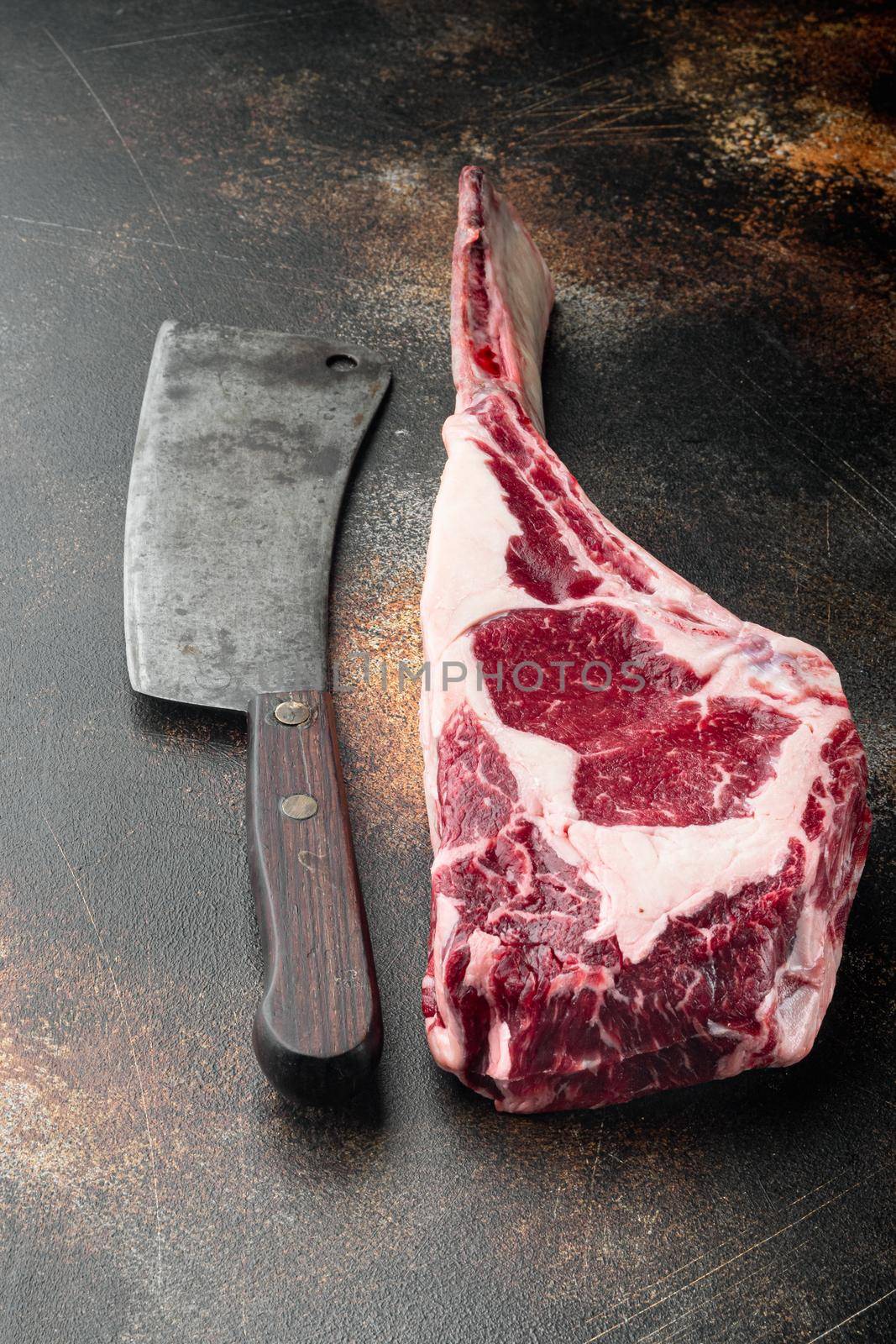 Dry aged raw tomahawk beef steak with ingredients for grilling, and old butcher cleaver knife, on old dark rustic background by Ilianesolenyi