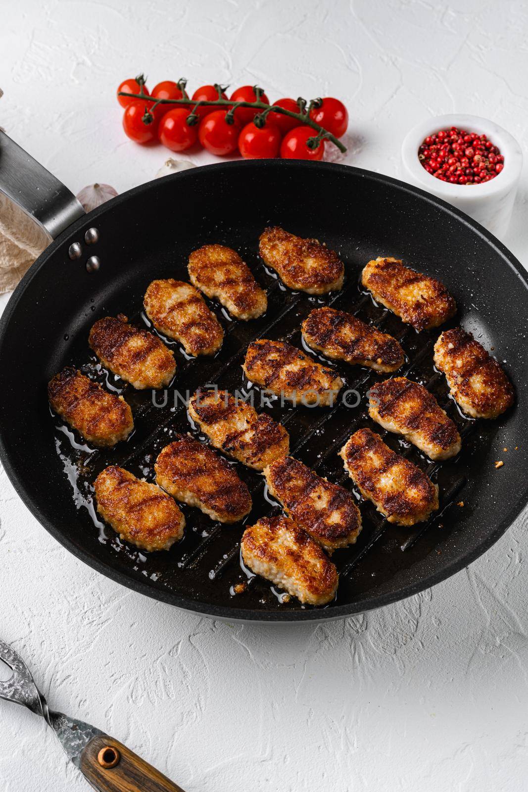 Golden chicken nuggets frying in hot oil, on white stone table background