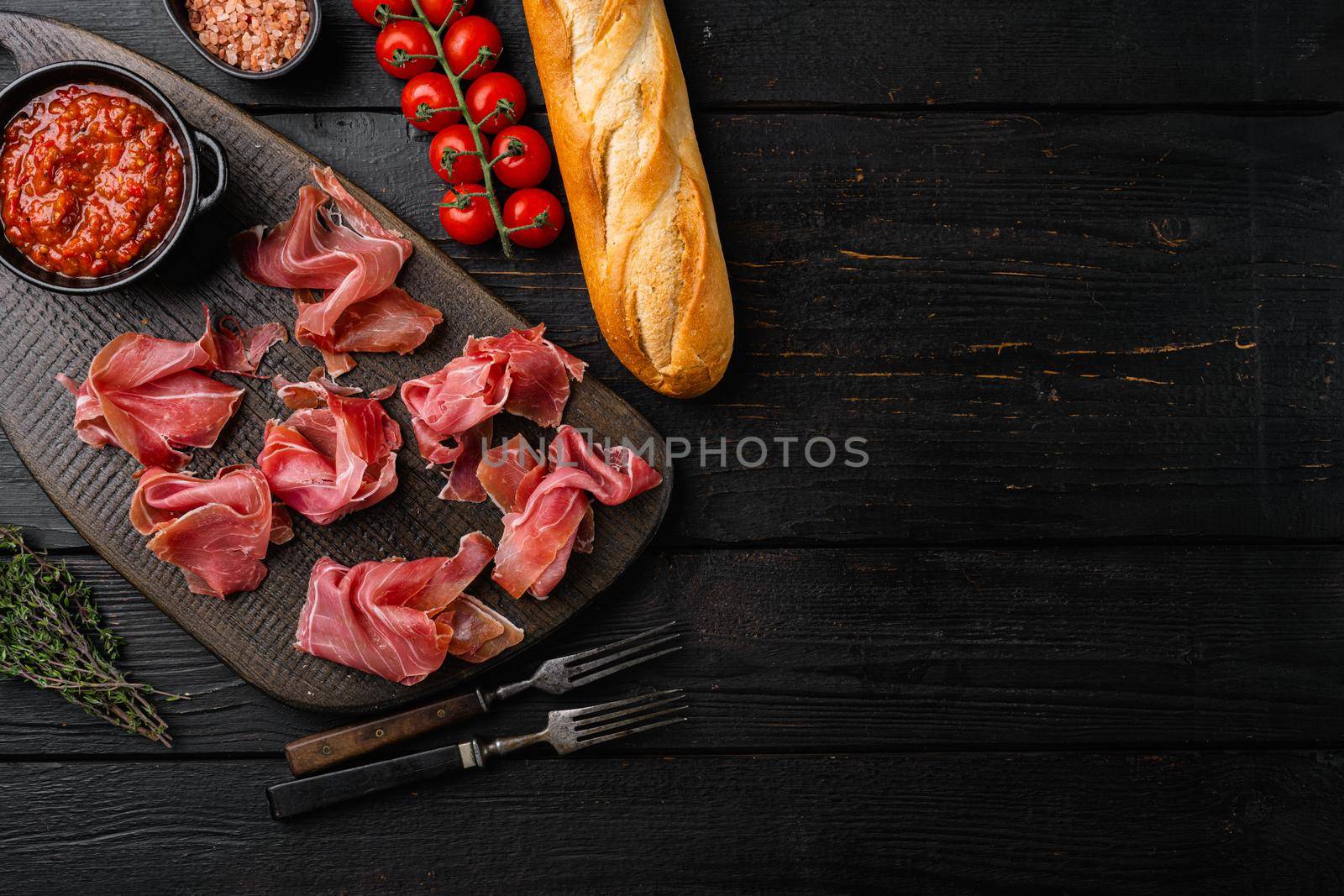 Slices of prosciutto di parma or jamon serrano set, on black wooden background, top view flat lay, with copy space for text by Ilianesolenyi