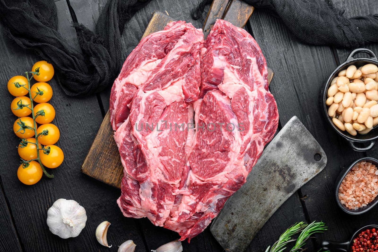 Legendary Ribeye fresh raw beef steak with spices and white beans set, and old butcher cleaver knife, on black wooden table background, top view flat lay