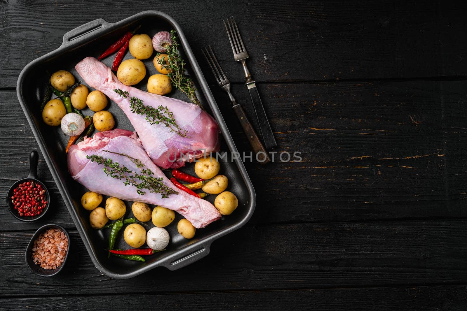 Fresh turkey legs with ingredients for cooking set, on black wooden table background, top view flat lay, with copy space for text