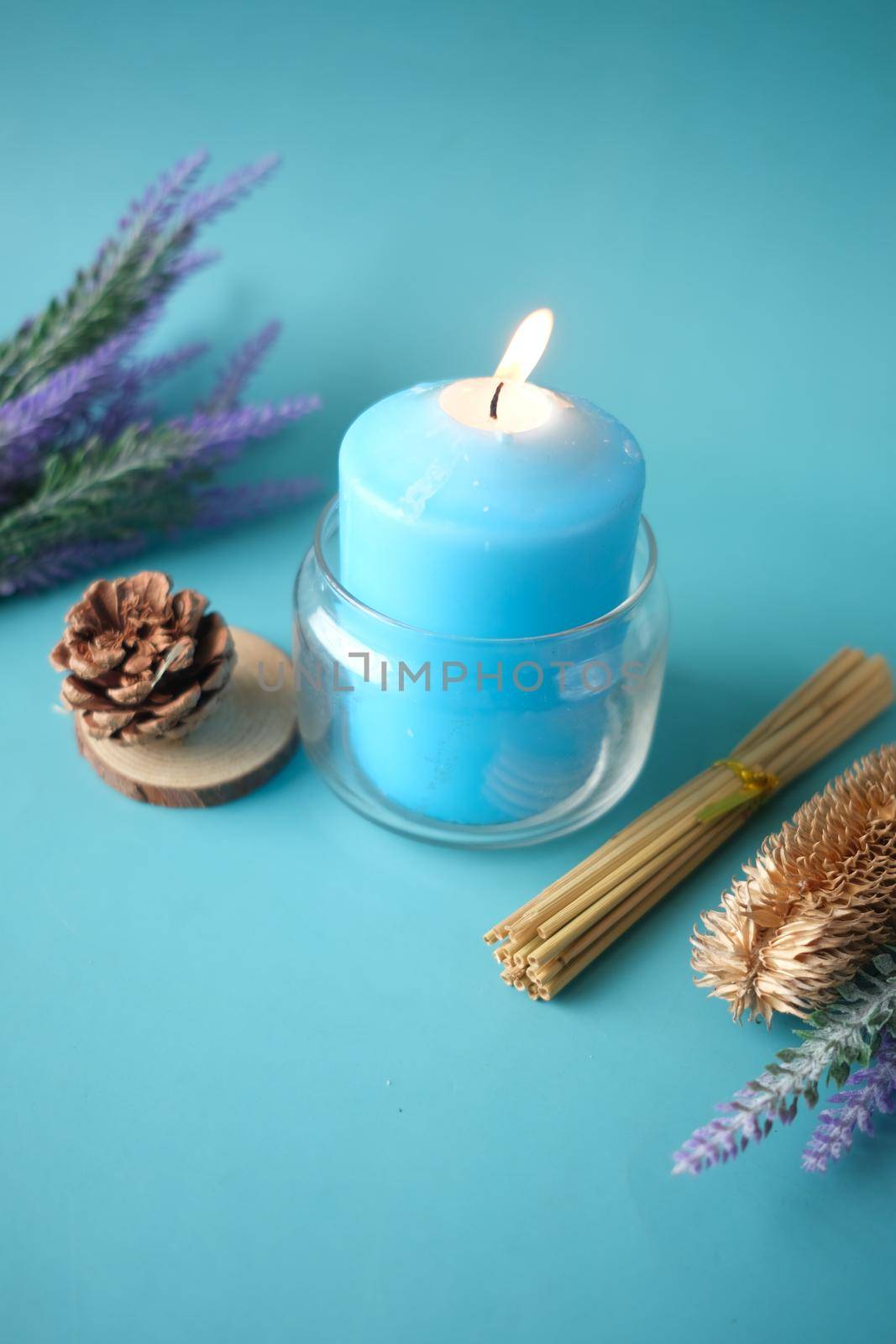 Natural candle in a glass jar and dried flowers on blue .