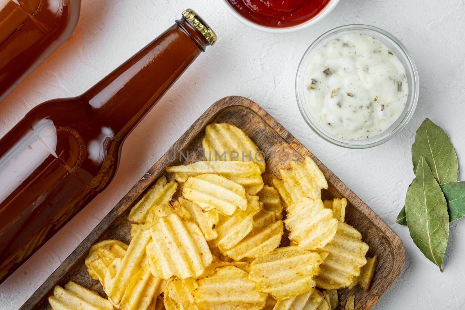 Crispy potato chips. Slices of potato, roasted with sea salt , with dipping sauces tomato dip sour cream, and bottle of beer , on white stone surface, top view flat lay by Ilianesolenyi