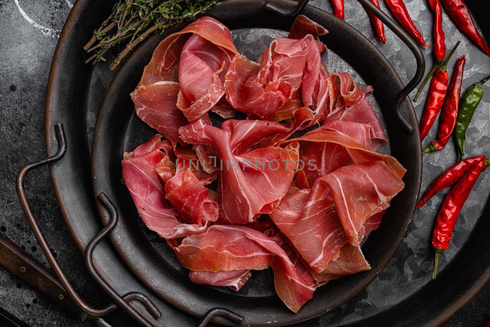 Slices of prosciutto di parma or jamon serrano, on black dark stone table background, top view flat lay