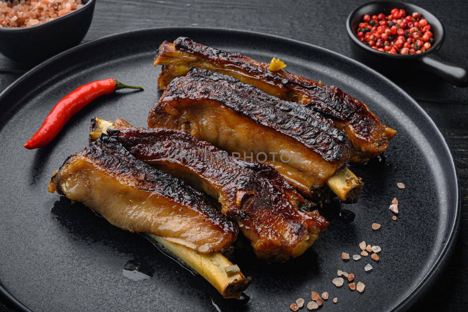 Grilled pork ribs with rosemary and honey set, on plate, on black wooden table background