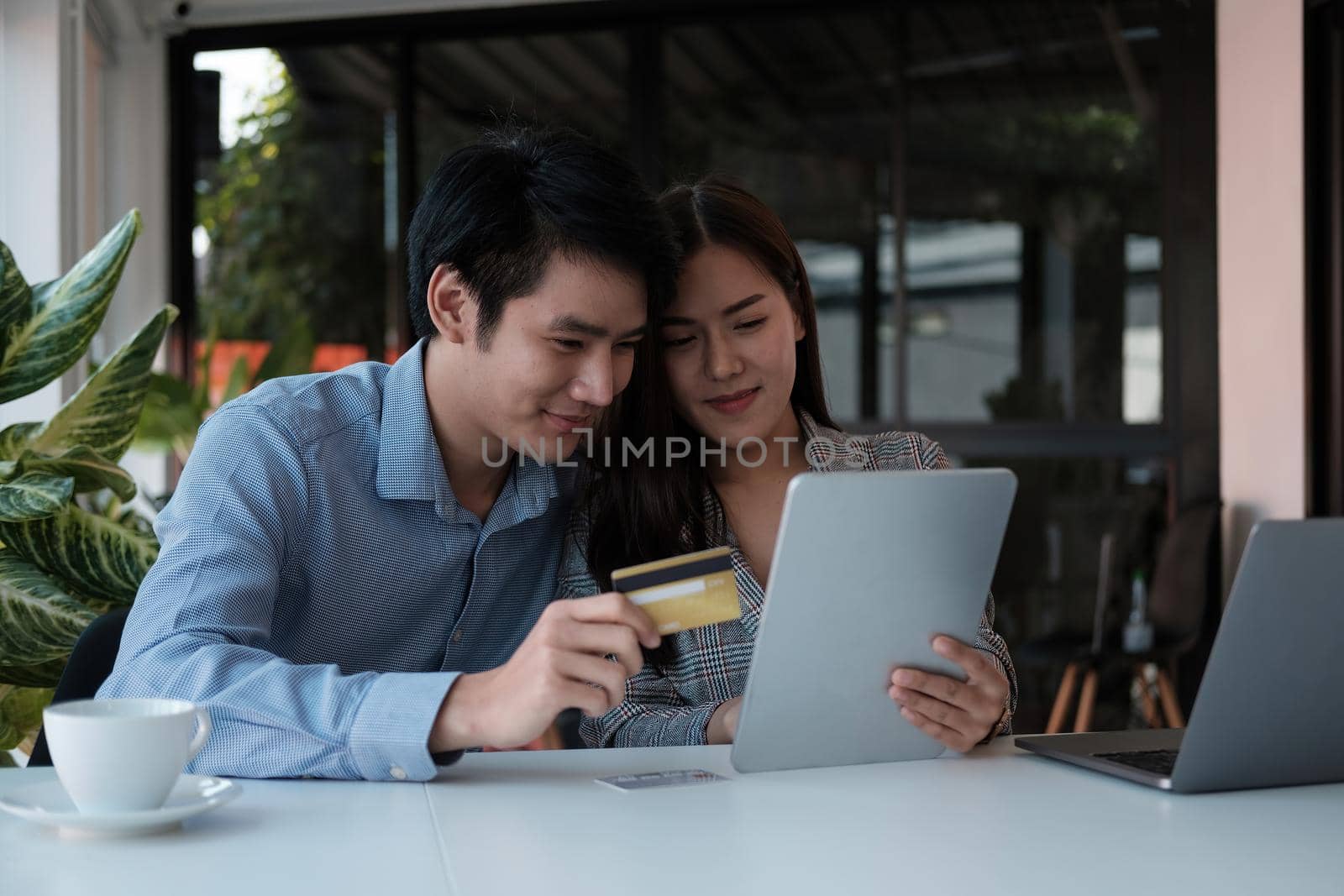 Asian couple at home shopping online with digital tablet and credit card.