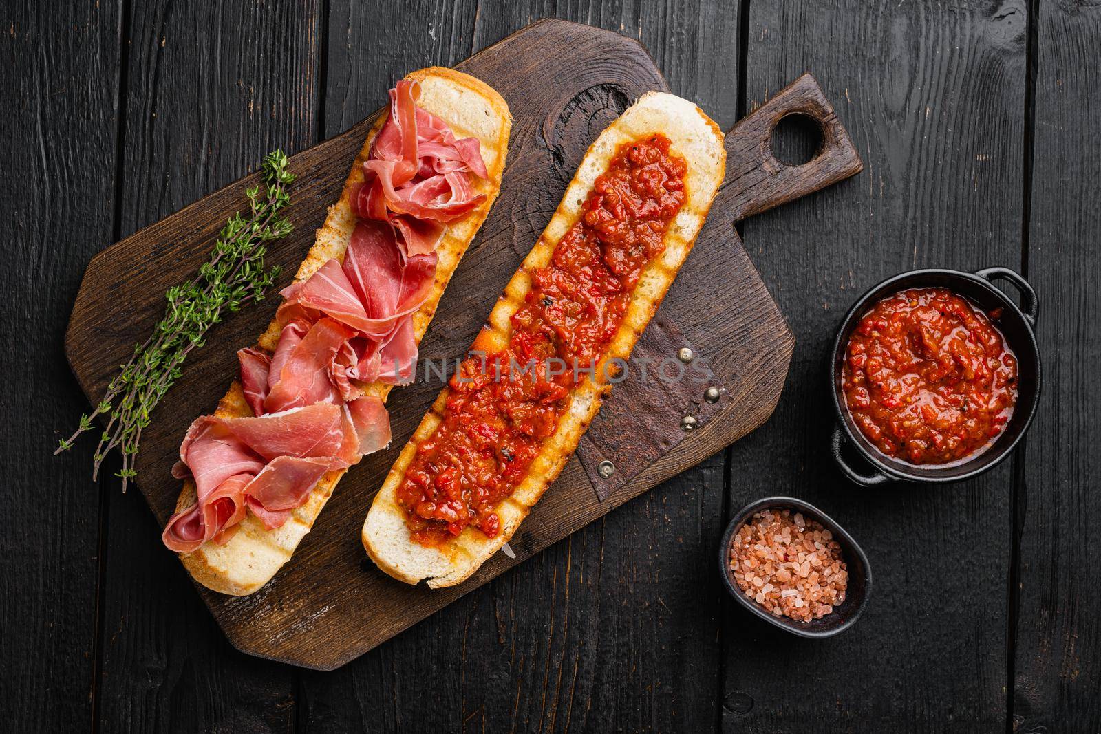 Crusty toast with fresh tomatoes and cured ham, on black wooden table background, top view flat lay