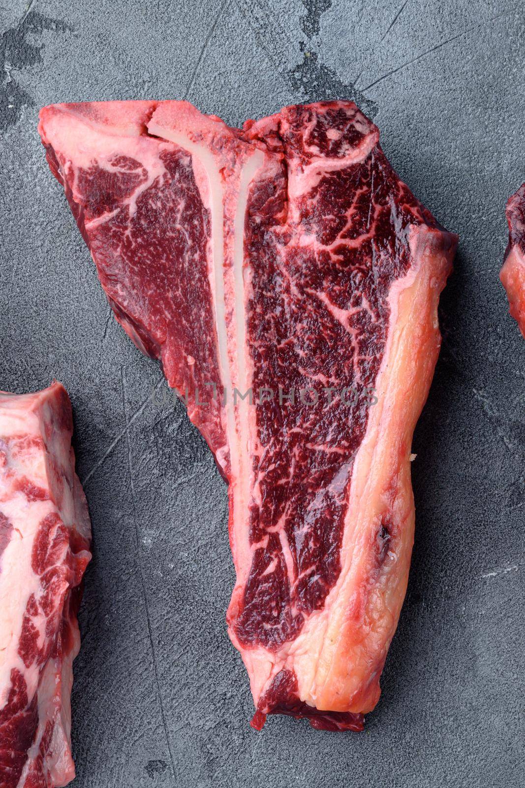 Prime cut tender raw t-bone steak for a BBQ, on gray stone background, top view flat lay by Ilianesolenyi