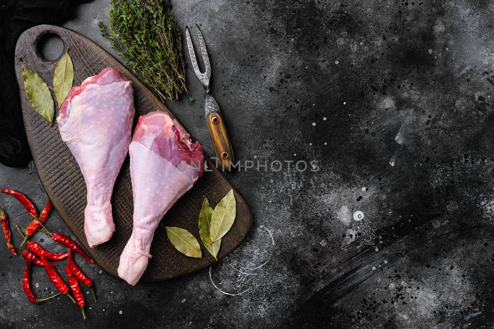 Turkey raw meat leg, on black dark stone table background, top view flat lay, with copy space for text