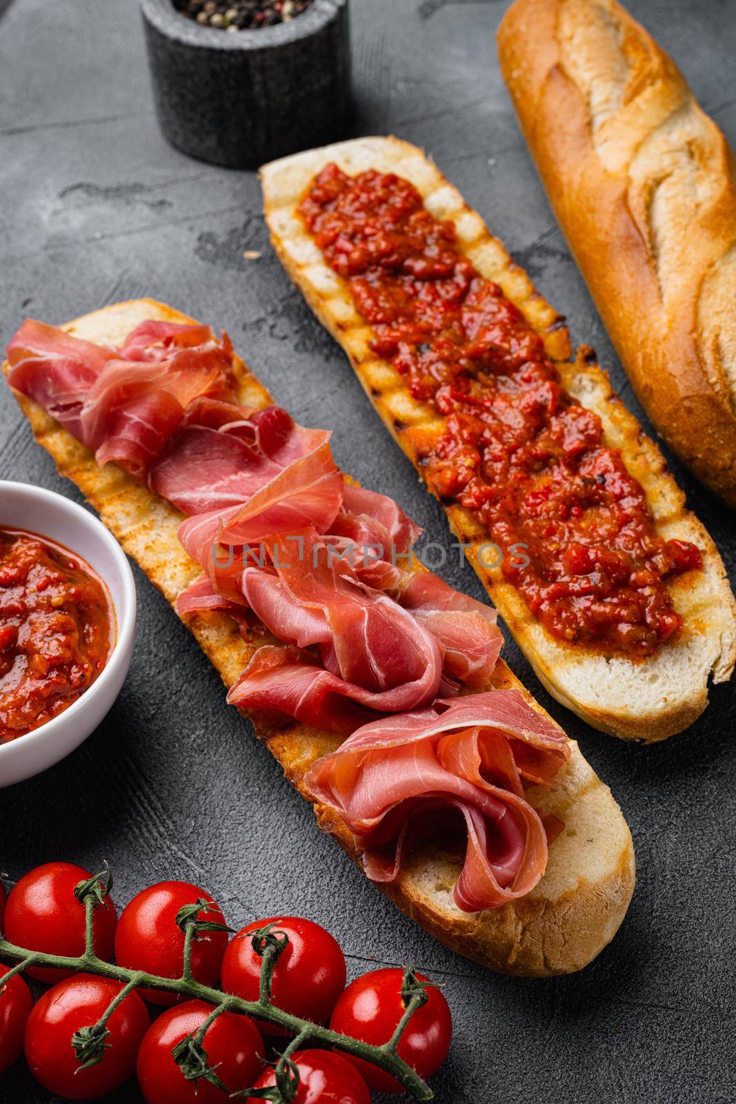 Toasted bread slice with fresh tomatoes and cured ham set, on gray stone table background