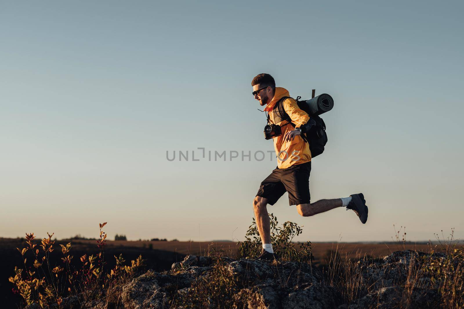 Travel Man Dressed in Windbreaker with Backpack and Camping Mat, Jumping on Top of Hill During Sunset, Male Nomad with Digital Camera Enjoy His Best Solo Trip