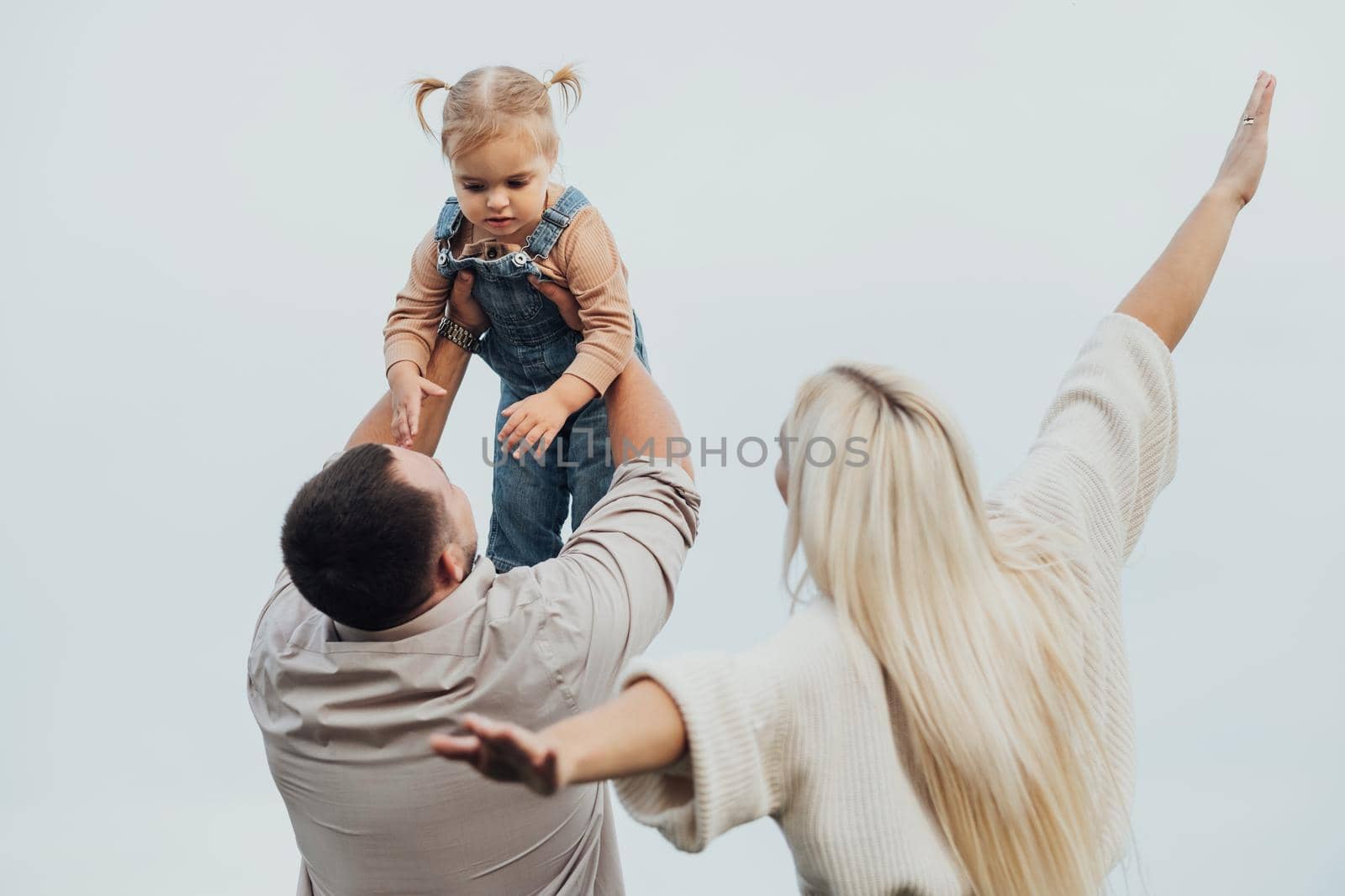 Young Family Having Fun Time Outdoors, Father Holding His Little Daughter in Arms Over Head, Mother Imitating Plane
