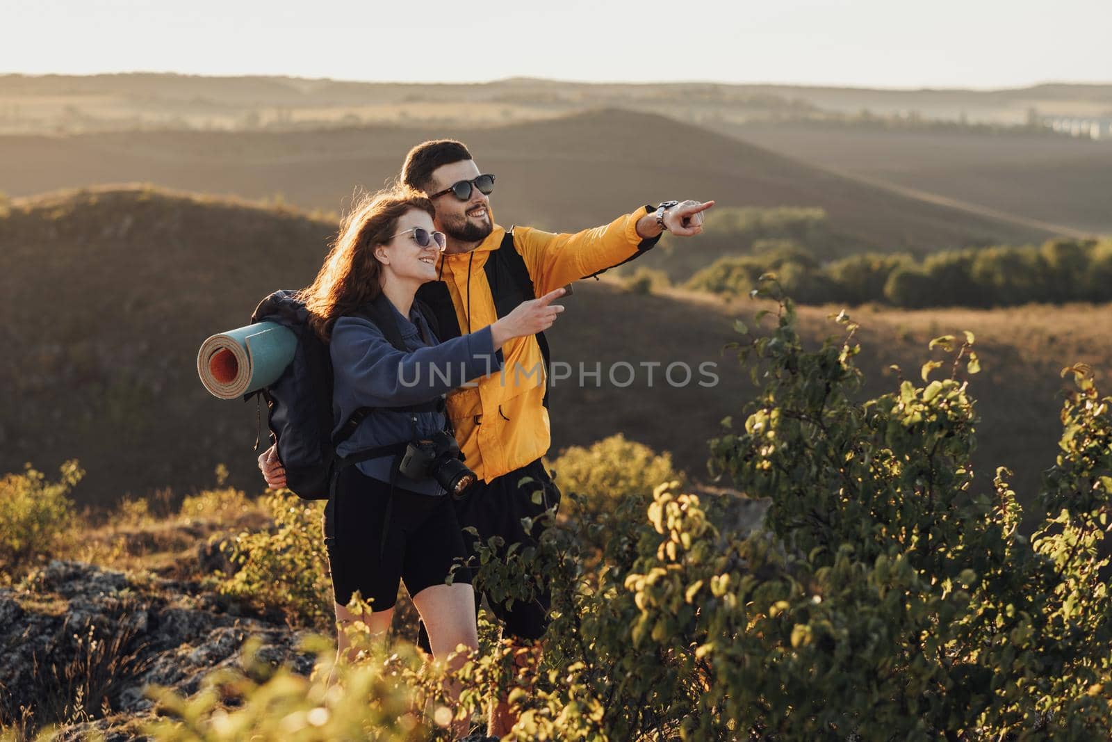 Happy Travelers Couple Man and Woman Hugging on the Top of Hill During Sunset and Showing Something That Surprised Them