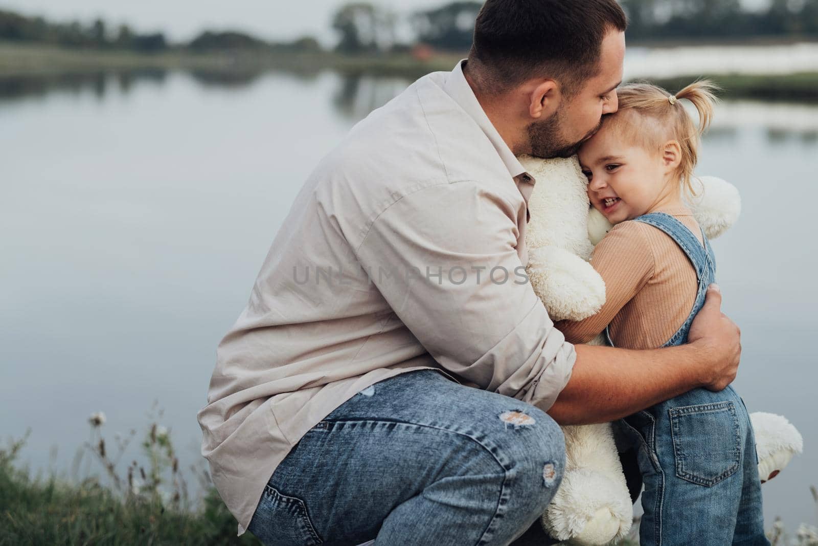 Young Father Hugging His Daughter and Gave Her Big Soft Toy Outdoors Near Lake