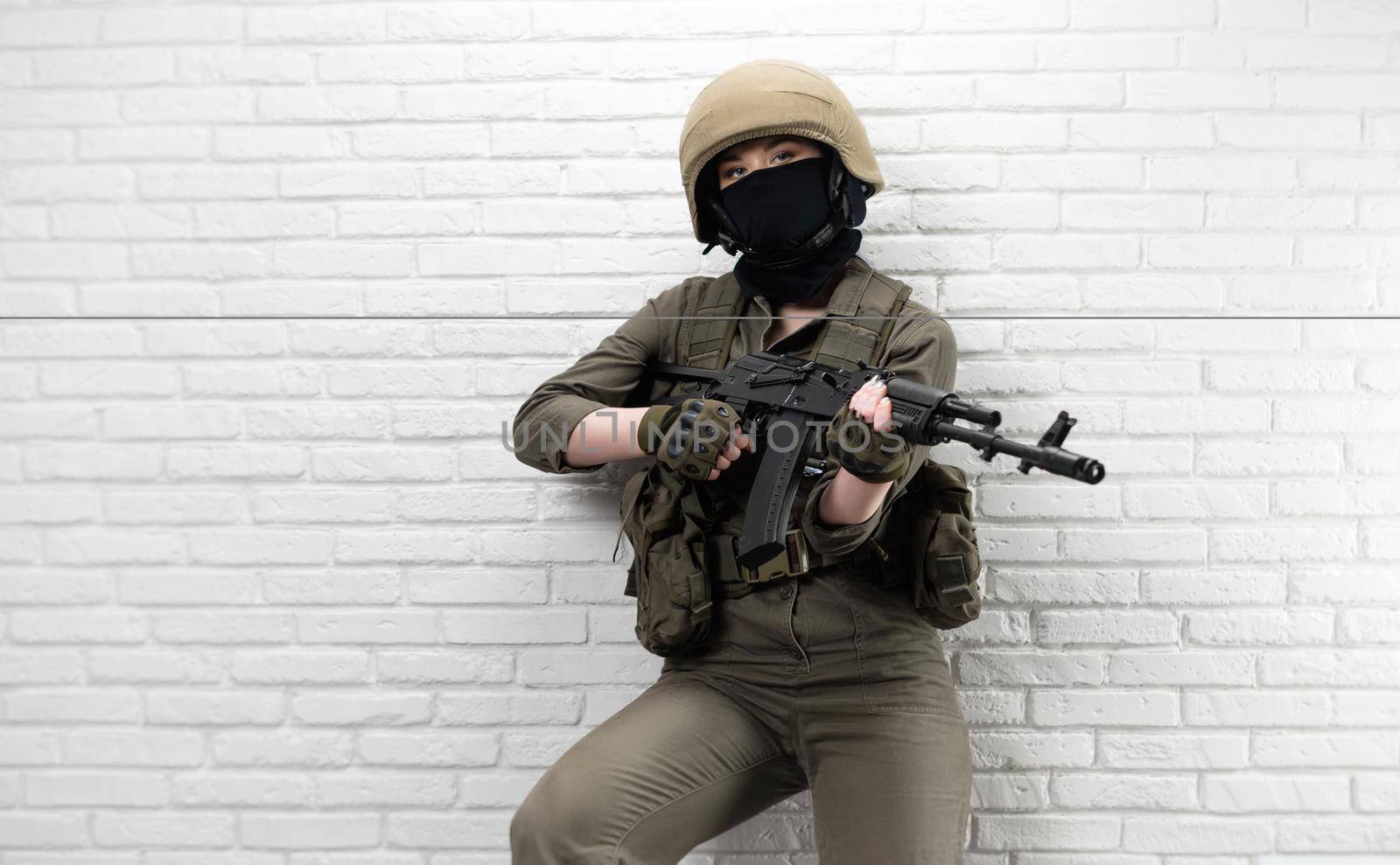A Ukrainian girl soldier in a helmet and military ammunition with a Kalashnikov assault rifle on the background of a brick wall by Rotozey
