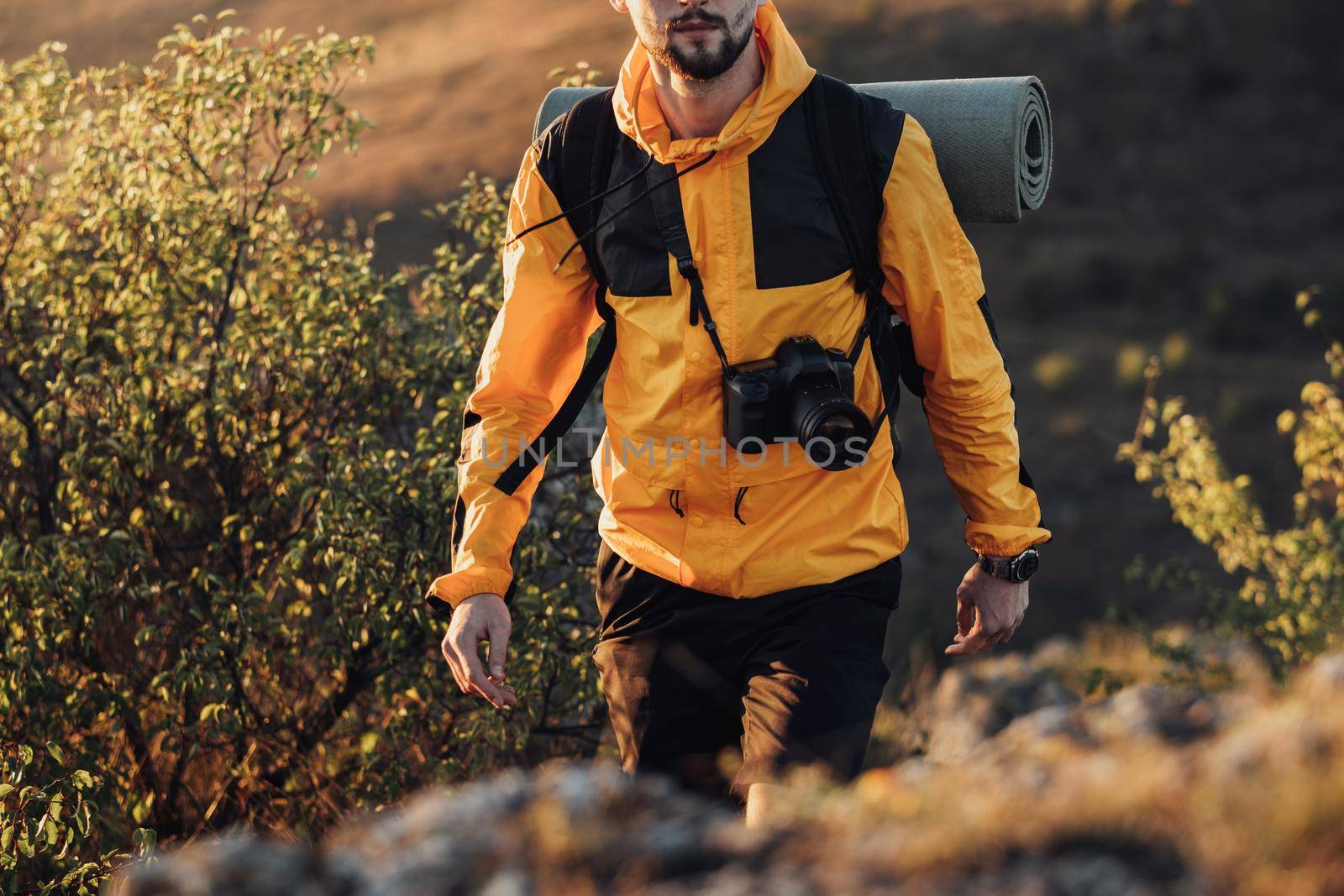 Unrecognisable Male Tourist Dressed in Windbreaker, Travel Man with Backpack and Camping Mat with Digital Camera Enjoy His Solo Trip Hiking on the Hill During Sunset by Romvy