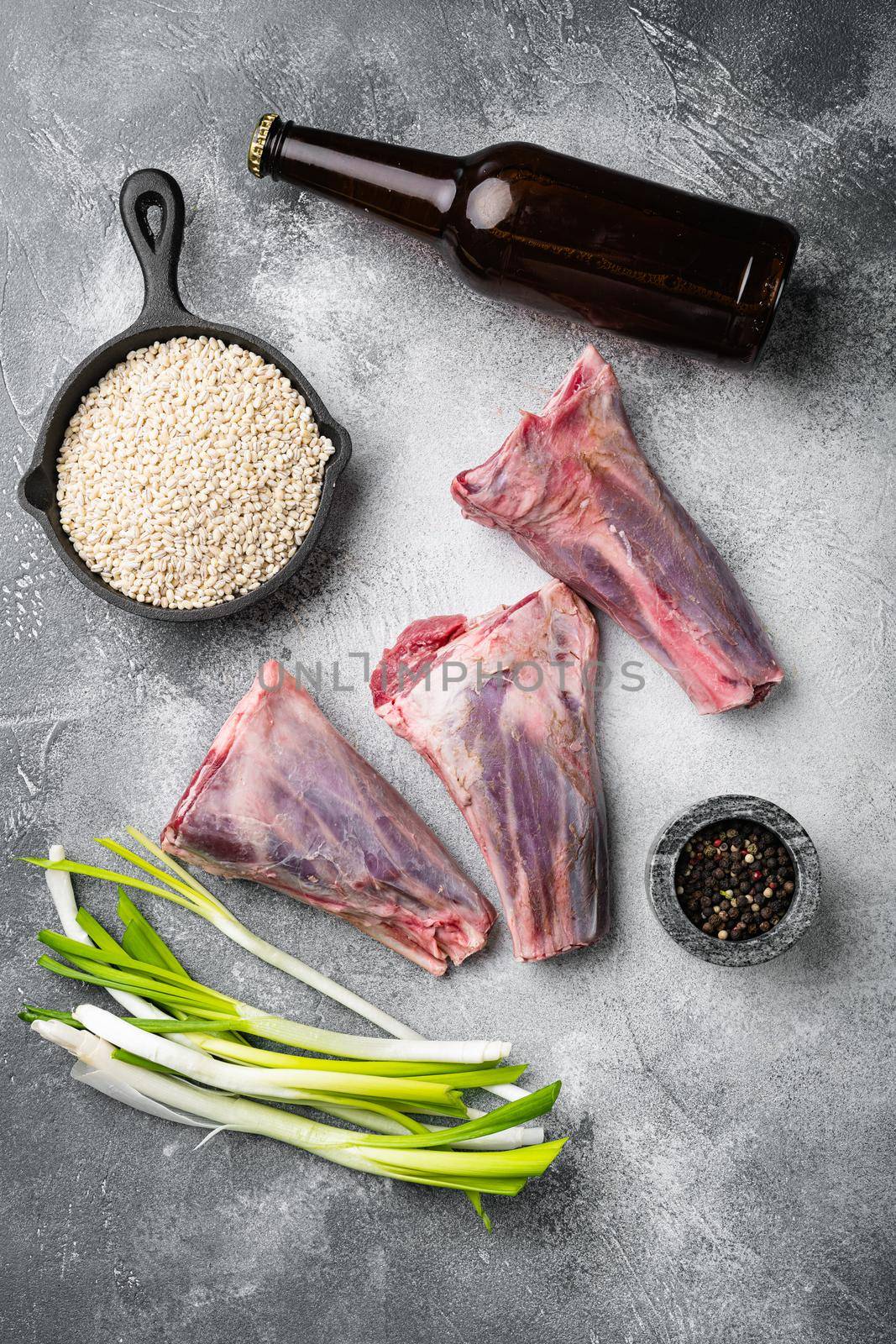 Raw lamb shanks with pearl barley and ale set, on gray stone table background, top view flat lay