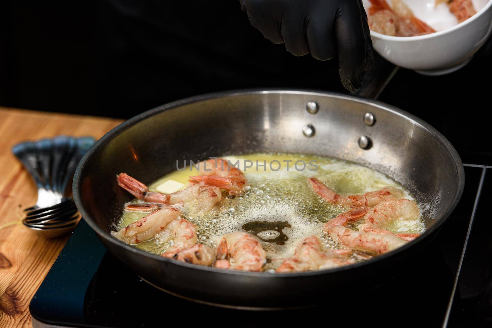 Fried red shrimps with garlic in olive oil on black pan on stove. by Ashtray25