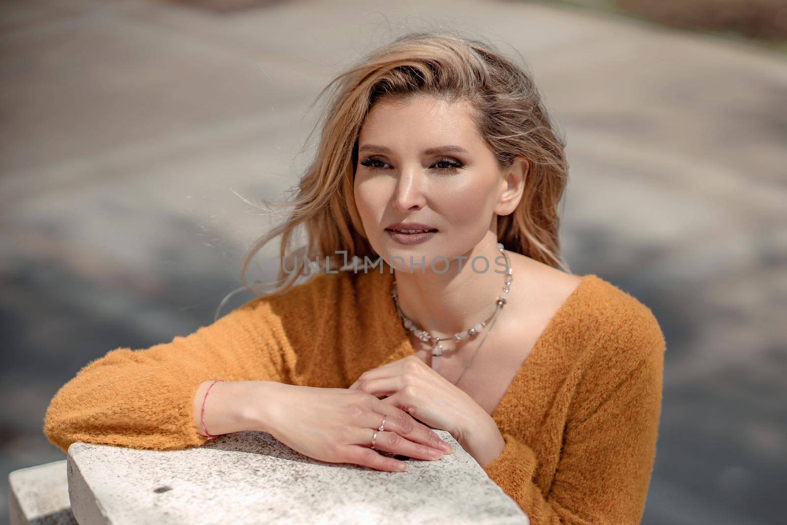 A middle-aged woman looks good blonde with curly beautiful hair and make-up on the background of the building. She looks into the camera. by Matiunina