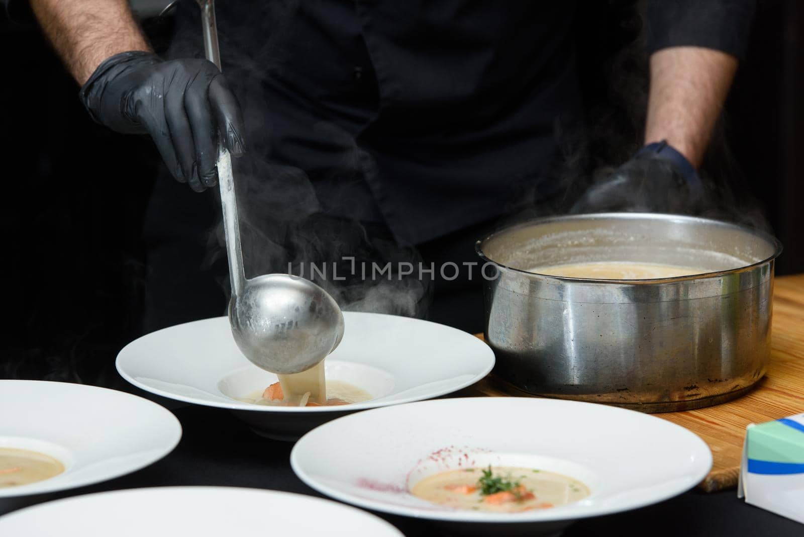 Chief cooking fish cream soup with salmon, cheese and herbs in white soup bowls by Ashtray25