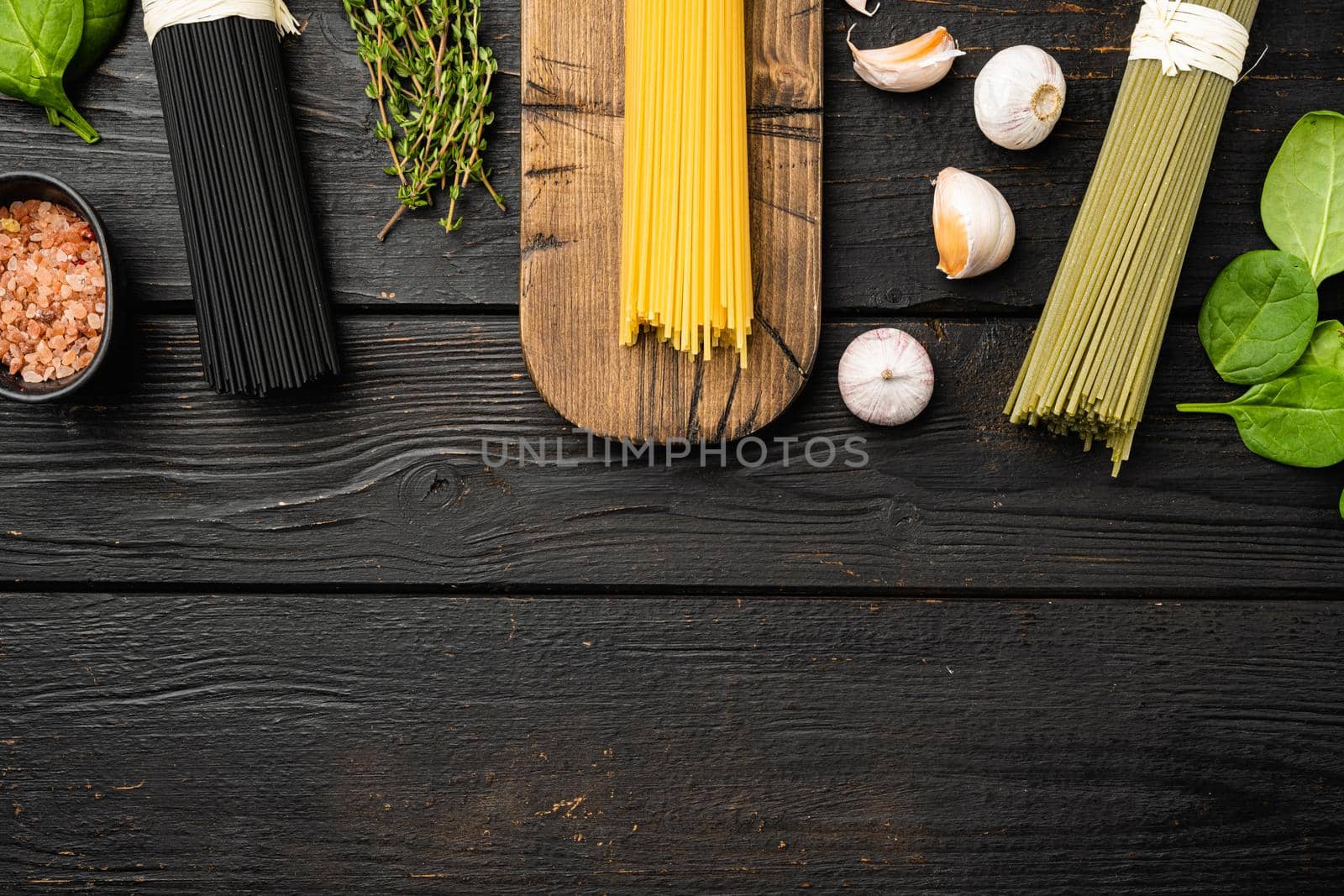 Dry colorful Italian pasta spaghetti with ingredients, on black wooden table background, top view flat lay, with copy space for text by Ilianesolenyi