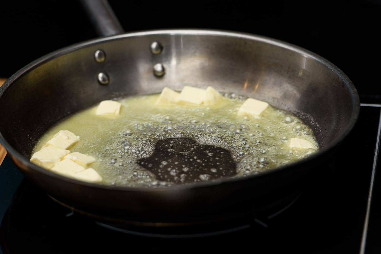 Pieceses of butter melted in a frying pan on a gas stove.