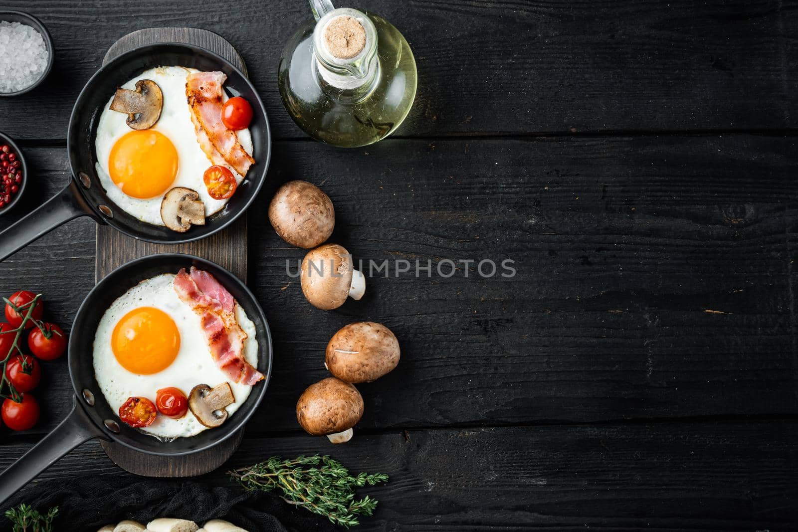 Fried eggs with bacon and vegetables set in cast iron frying pan, on black wooden table background, top view flat lay , with space for text copyspace