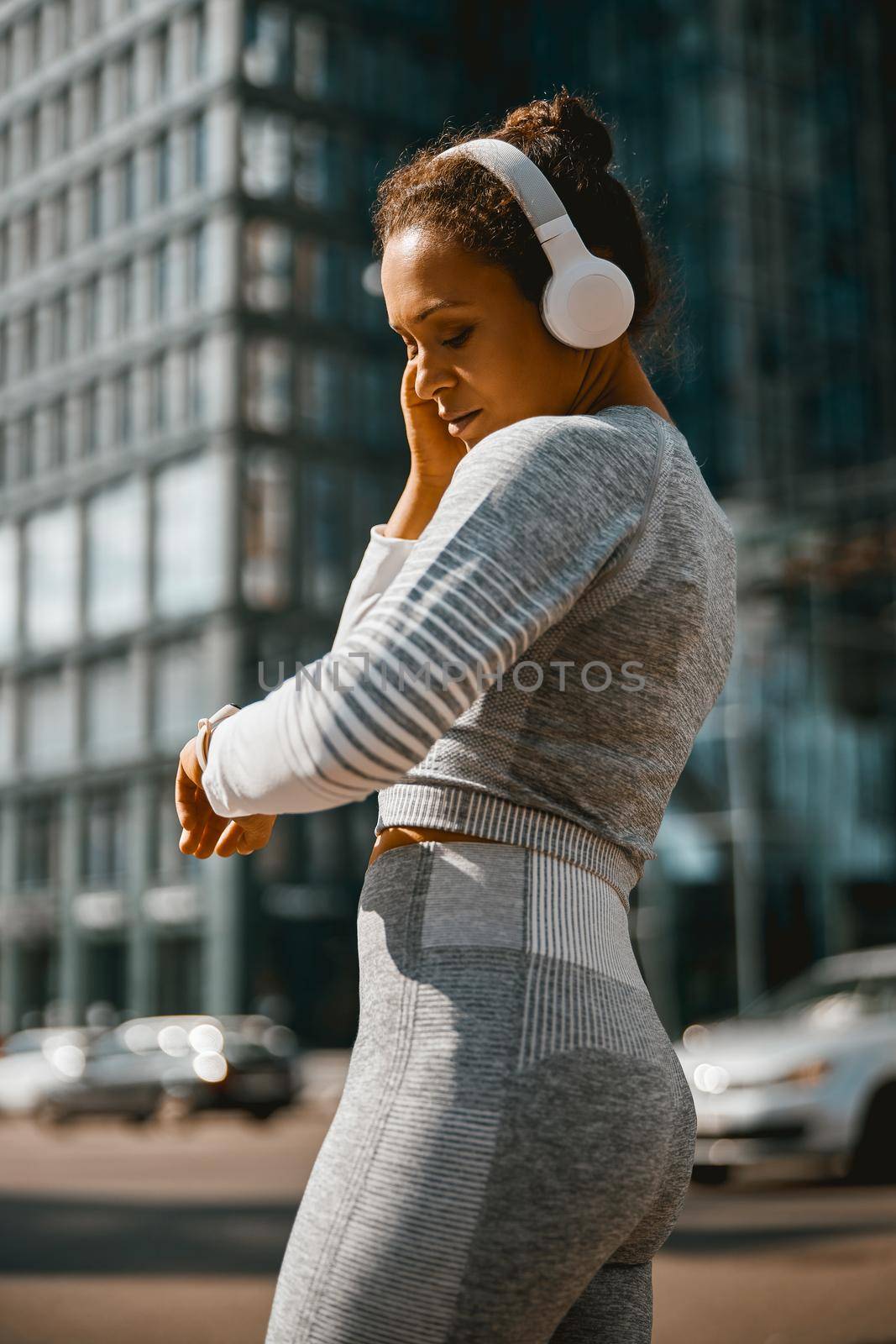 Busy athletic woman in headphones checking time on smartwatch by Yaroslav_astakhov