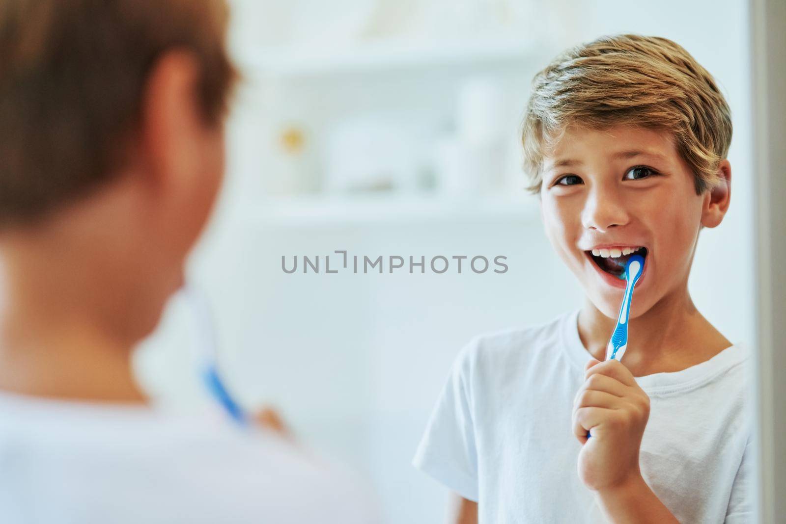 Keeping my teeth strong. Shot of a cheerful young boy looking at his reflection in a mirror while brushing his teeth in the bathroom at home during the day. by YuriArcurs