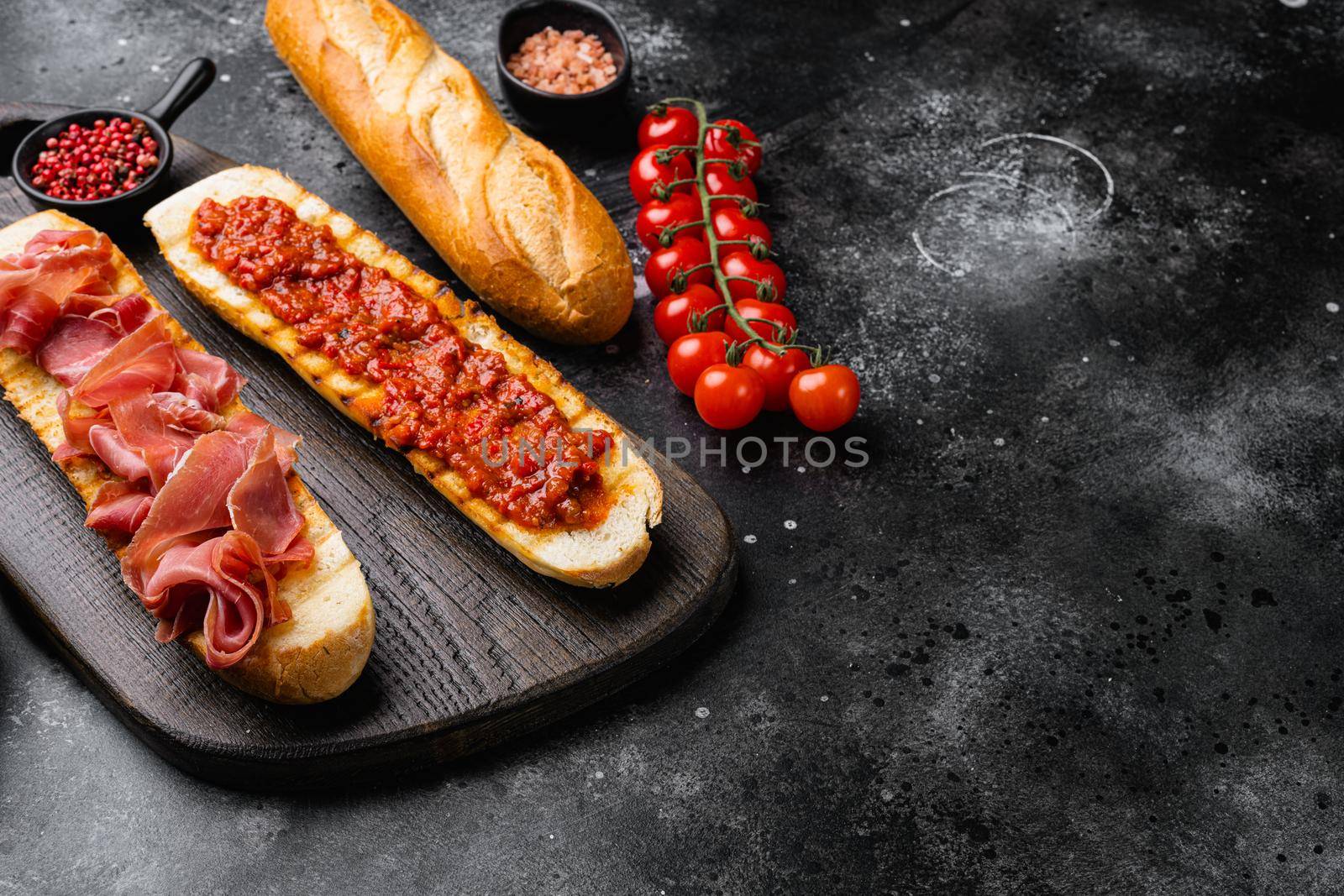 Toasted bread slice with fresh tomatoes and cured ham set, on black dark stone table background, with copy space for text