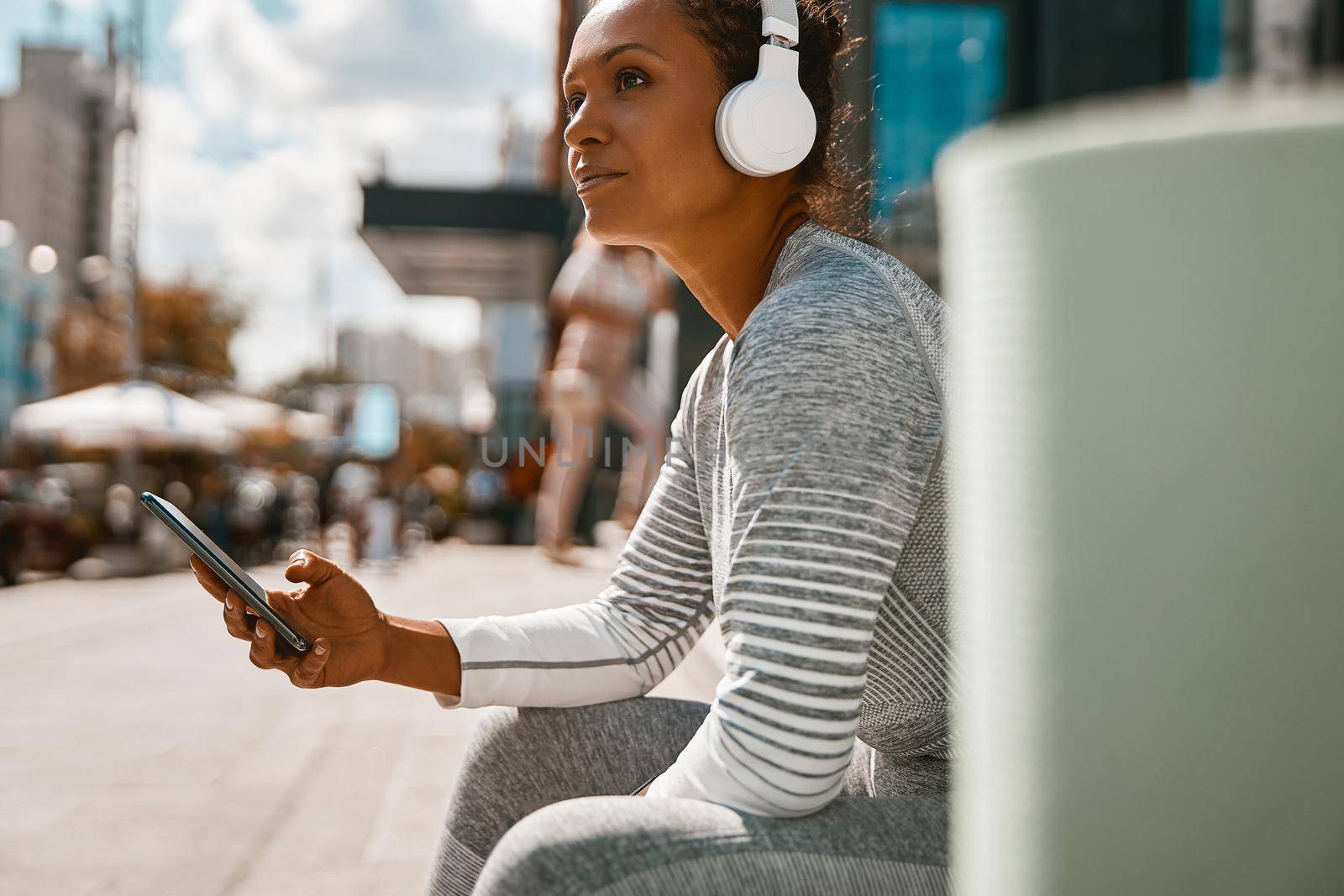 Sportive woman sitting outdoors on a sunny day after training. Sports, technology, active lifestyle