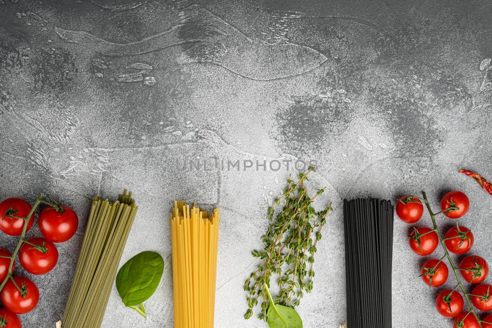 Multi colored spaghetti with ingredients set, on gray stone table background, top view flat lay, with copy space for text