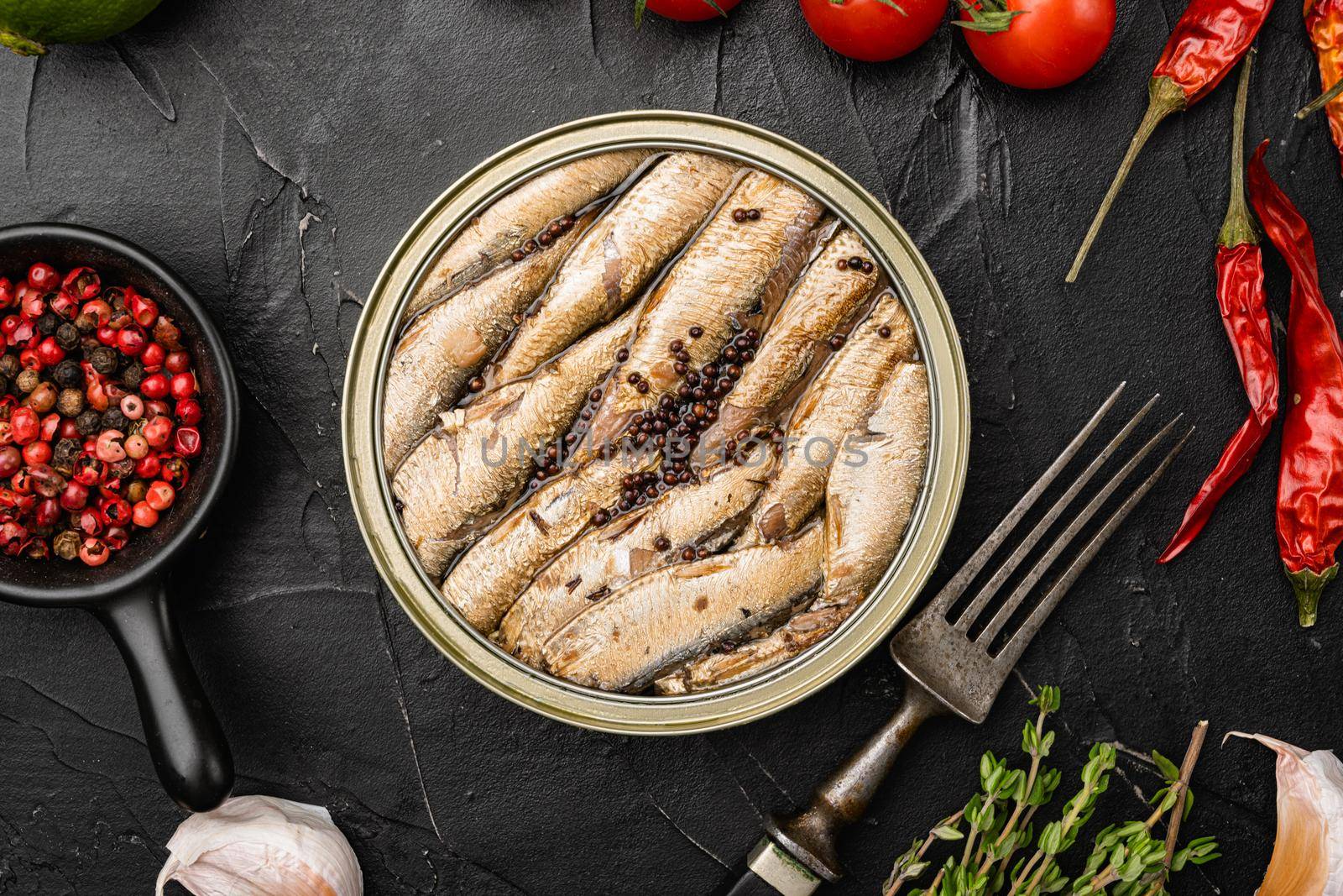 Tasty smoked fish, canned sardines in oil set, on black dark stone table background, top view flat lay