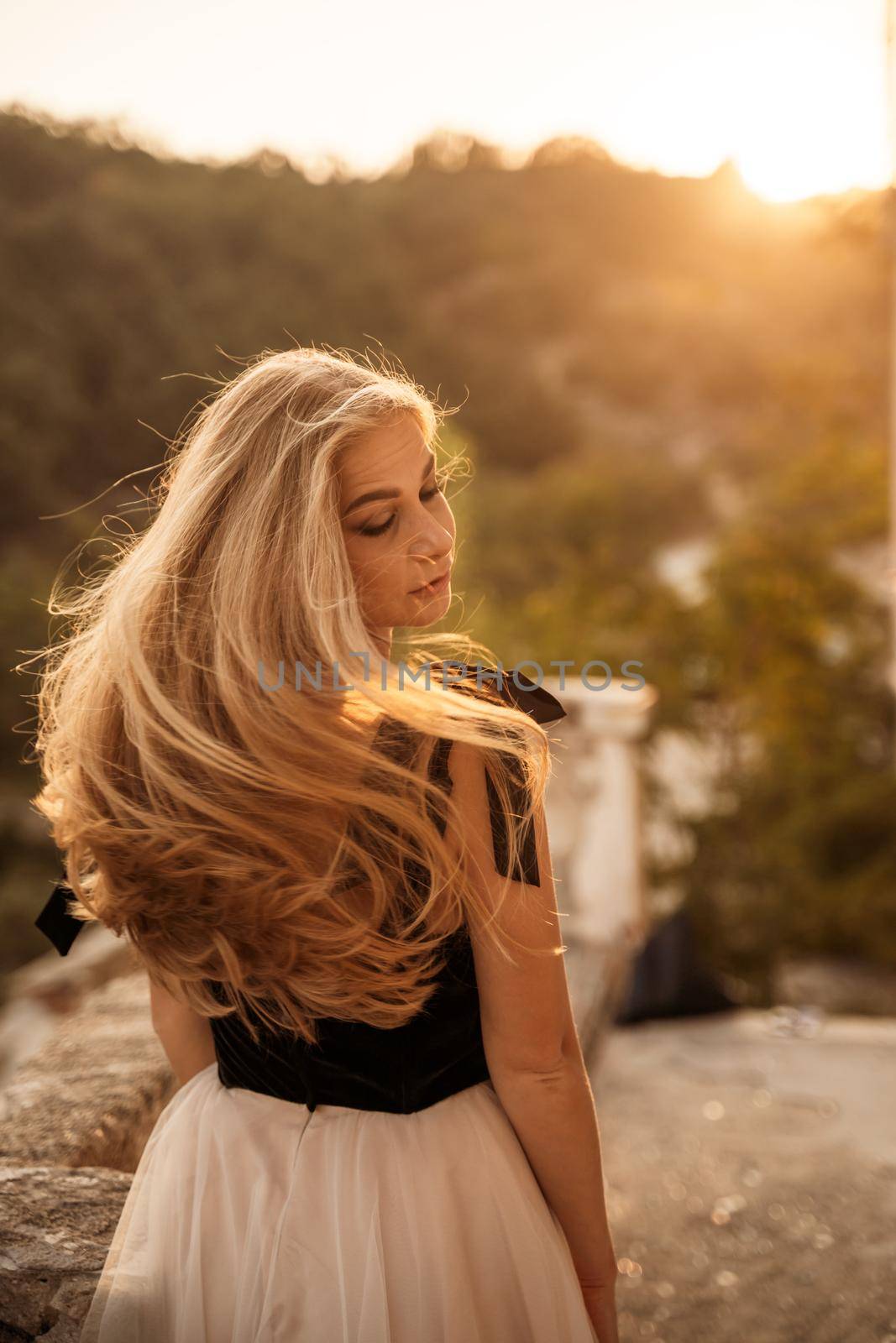 Blonde long hair, nature summer happy adult girl with long blond hair developing in the wind in nature. Dressed in a black top, white skirt. by Matiunina