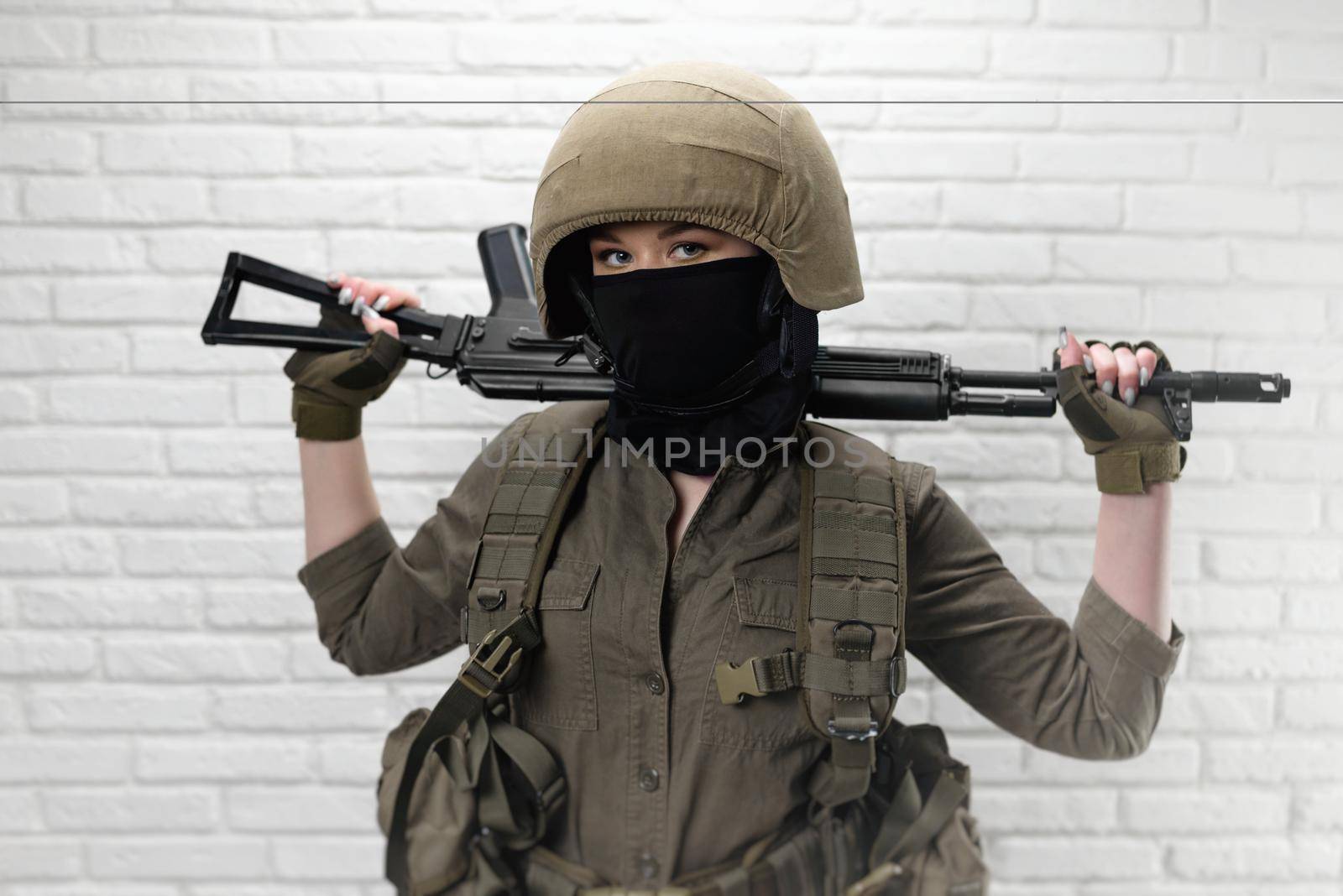 A Ukrainian girl soldier in a helmet and military ammunition with a Kalashnikov assault rifle on the background of a brick wall by Rotozey