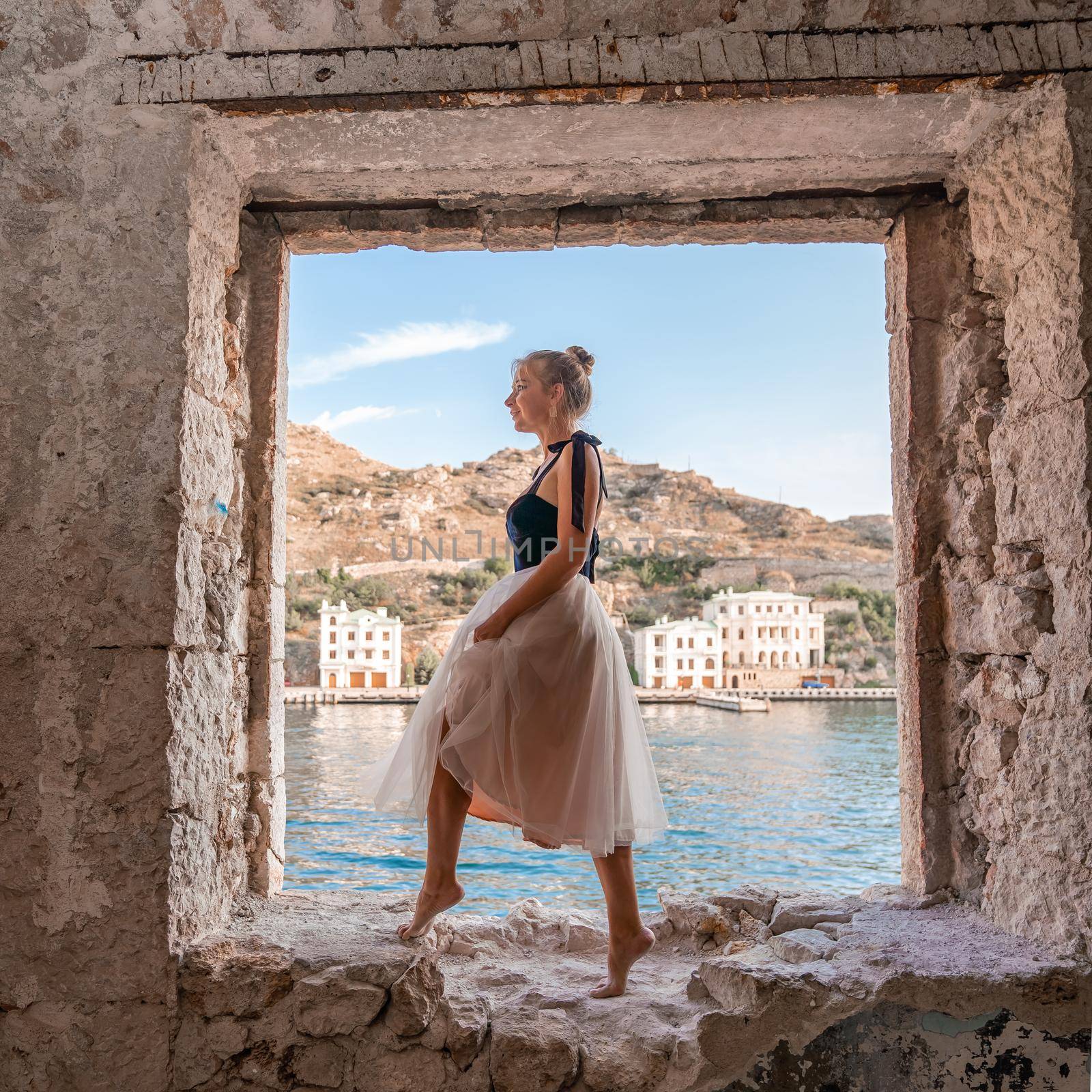 Side view portrait of a relaxed woman breathing fresh air at the seaside. She stands on the window in the old building