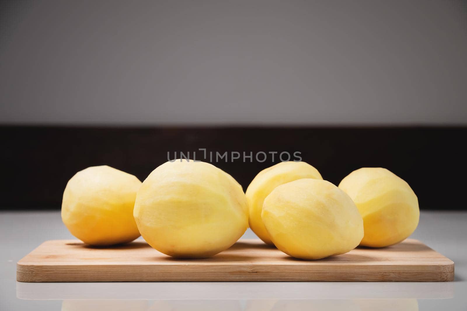 Close-up Several peeled potatoes on a wooden cutting board on a white table. by yanik88