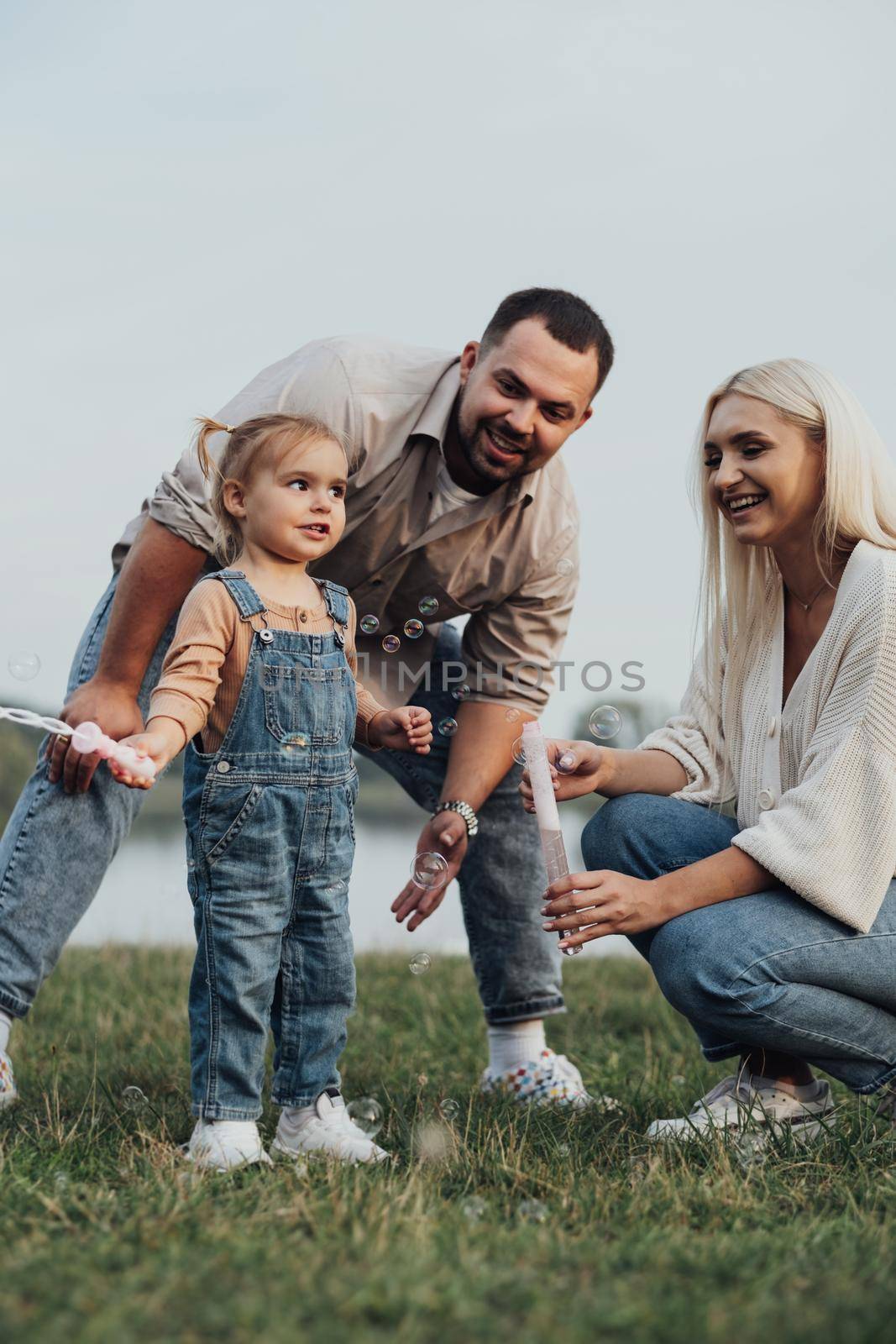 Portrait of Happy Young Family, Mom and Dad with Their Little Daughter Having Fun Outdoors Outside the City by Romvy